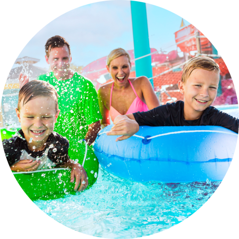 A family of four enjoys a fun day at the water park, playing and splashing in the pool together.