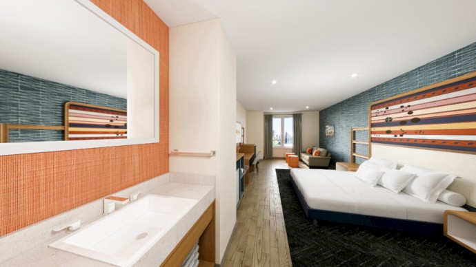 A modern hotel room with a spacious bathroom, a large bed, a seating area, a desk, and contemporary decor, featuring warm and cool tones.