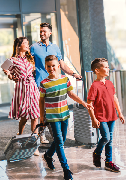 A family of four, with parents and two children, are walking through an airport with their luggage, appearing happy and ready for travel.